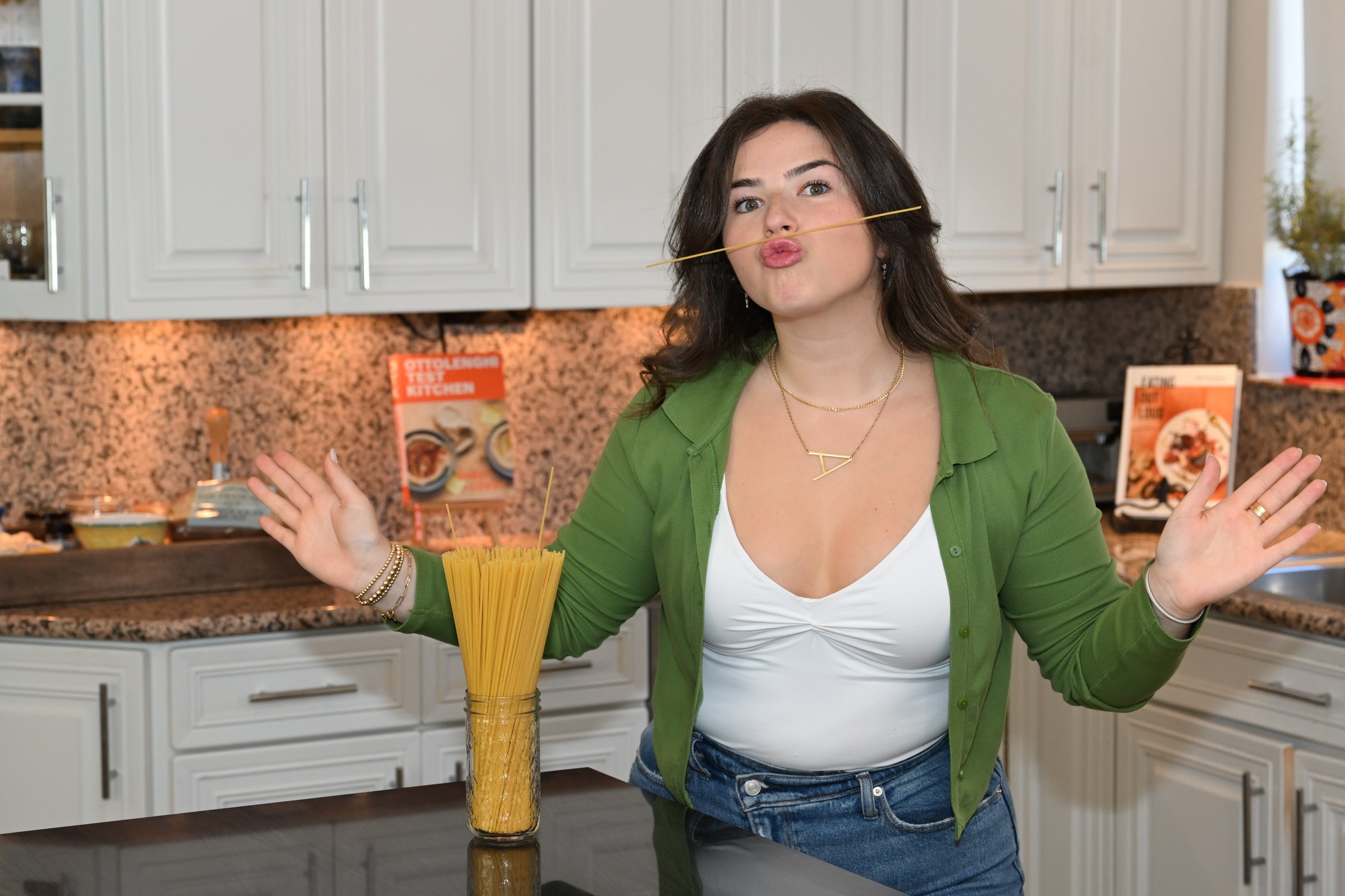 Woman playfully holding a spaghetti stick in her mouth in a kitchen.