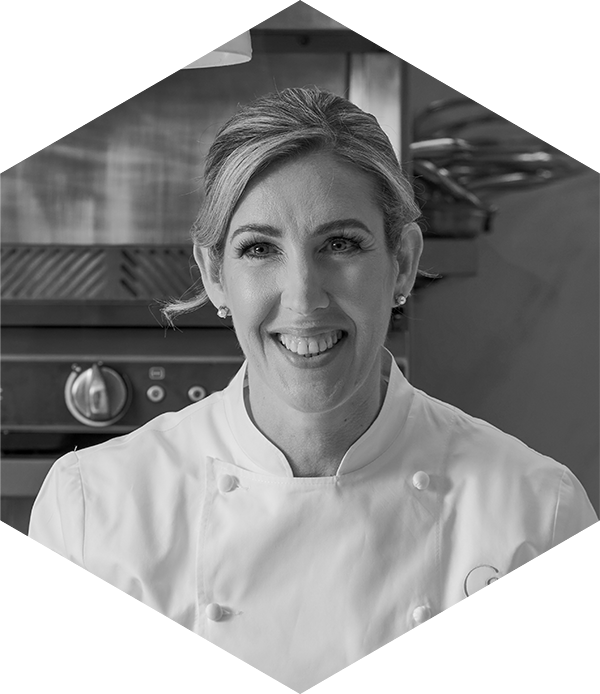 Smiling chef in a kitchen setting, wearing a white chef's coat.