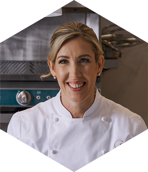 Smiling chef in a white coat standing in a professional kitchen.