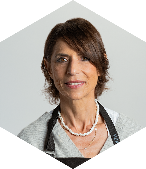 Portrait of a woman with short brown hair, wearing a pearl necklace, against a plain background.