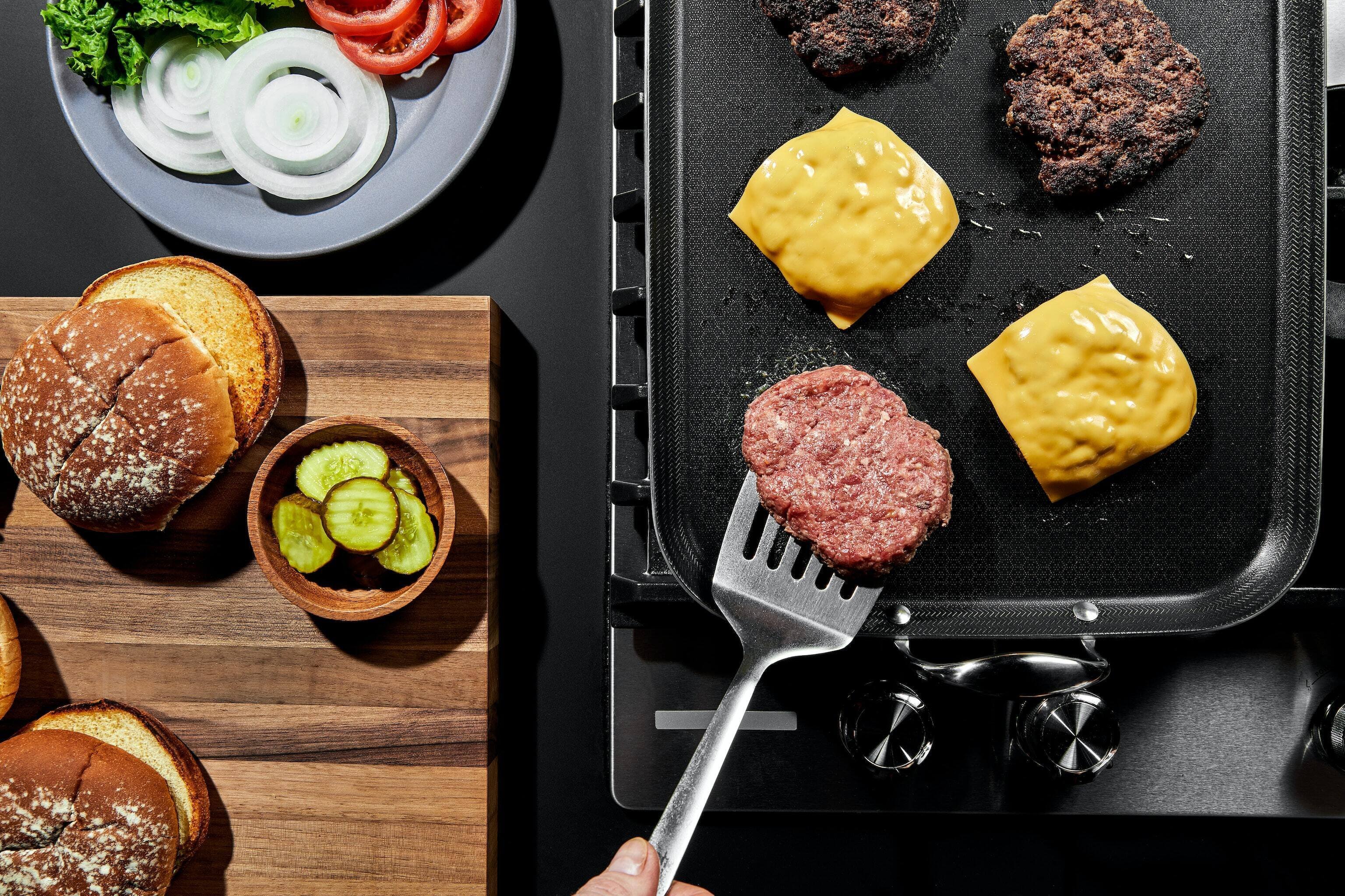 Craft the perfect burger with our Hybrid Double-Burner Griddle. Experience even cooking with its tri-ply construction, accompanied by fresh ingredients for a gourmet meal at home.