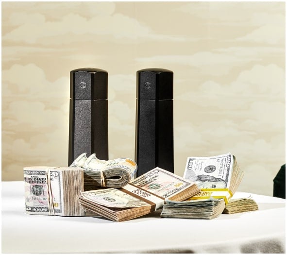 Bundles of U.S. currency on a table with two black cylindrical objects in the background.