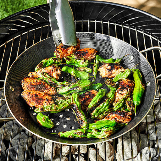 Grilled chicken and green peppers in a pan on an outdoor barbecue grill.