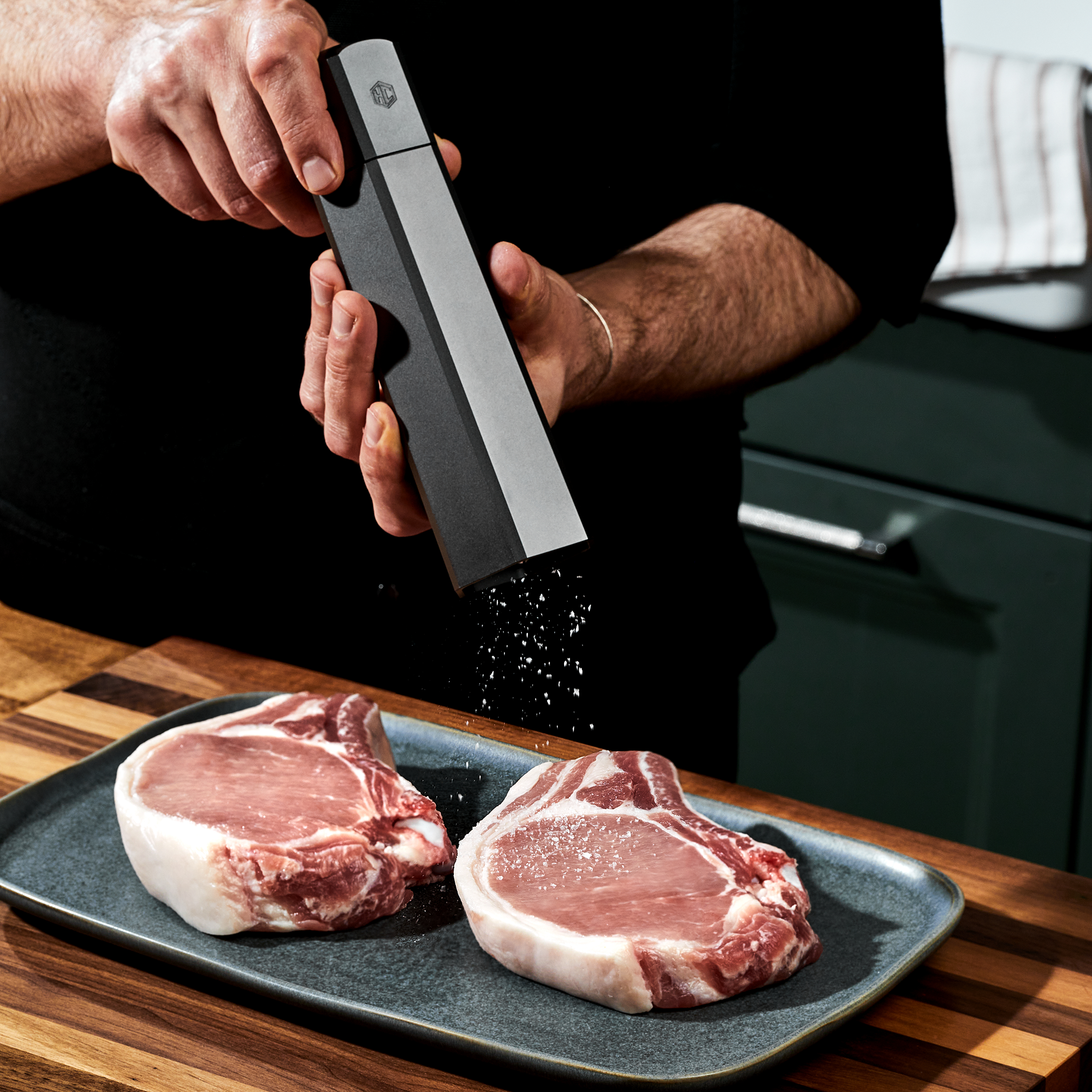 Person seasoning raw pork chops with salt in the kitchen.