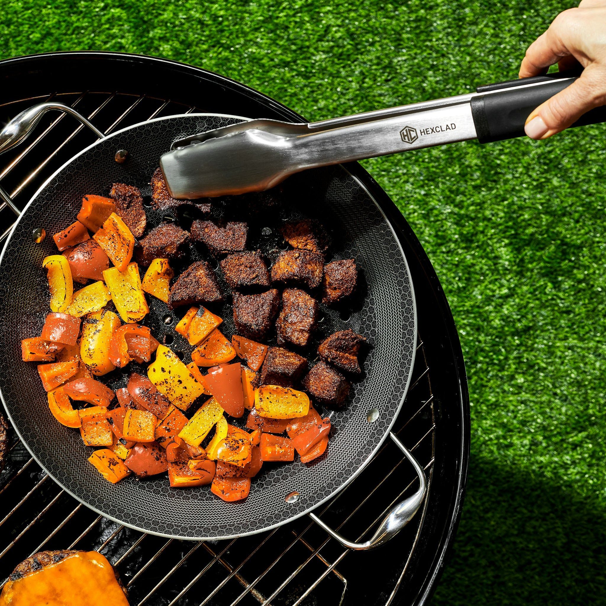 Grilled vegetables and meat in a HexClad pan on a barbecue grill.