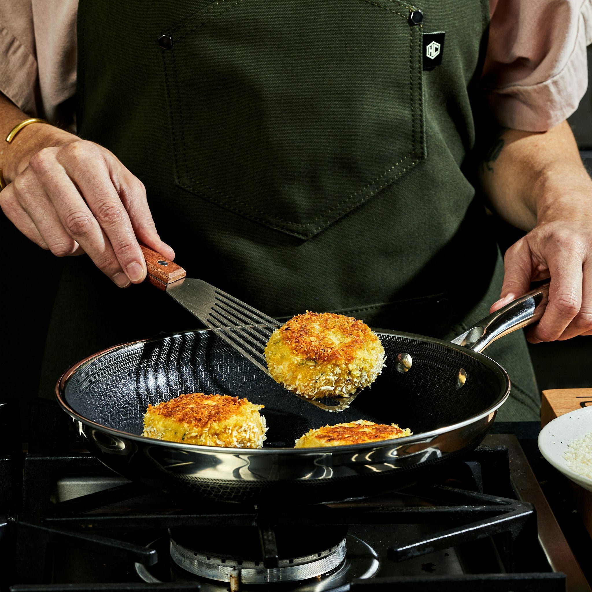 Person frying breaded patties in a pan wearing a green apron.