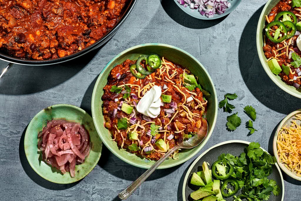Weeknight chili in a bowl with toppings around it