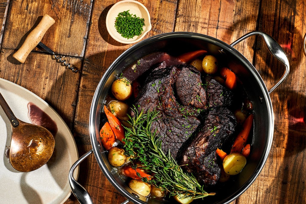 pot with meat and potatoes in it sitting on a wood surface