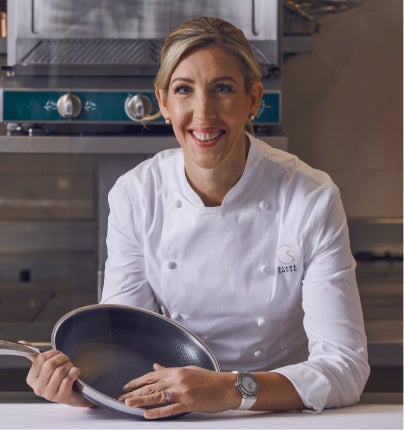 A chef in a white uniform holds a frying pan in a professional kitchen.