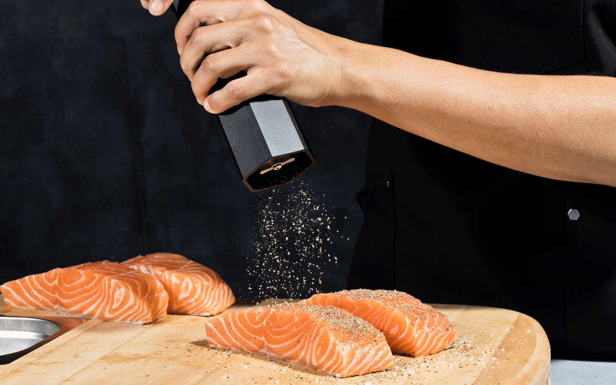 Seasoning fresh salmon with black pepper on a wooden cutting board.