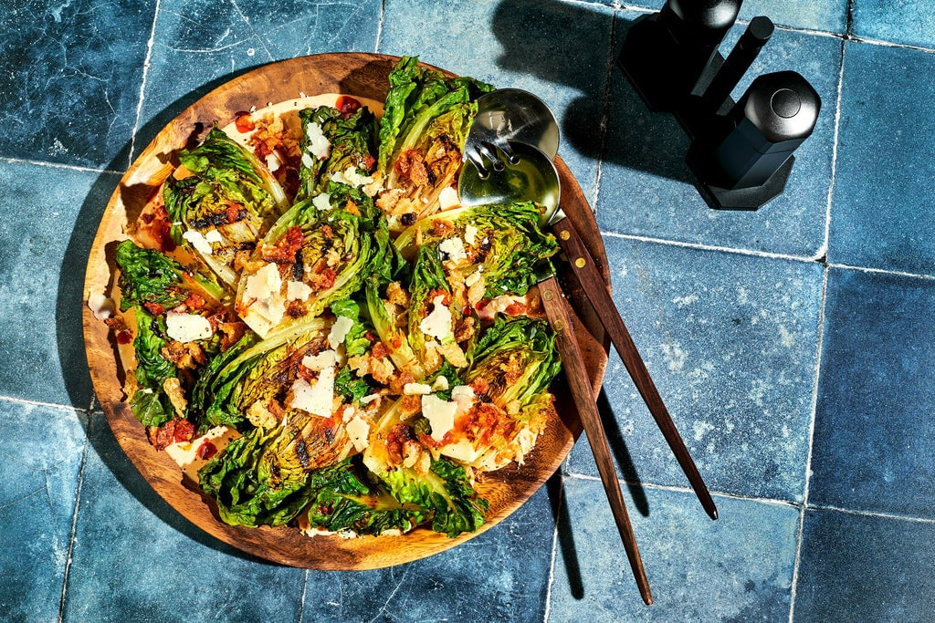 Grilled Little Gem Salad with Calabrian Chile Caesar in bowl against blue background