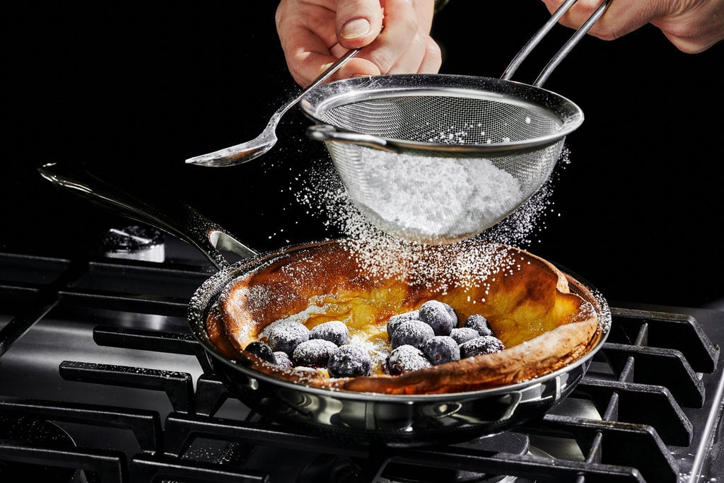 Powdered sugar is added to a pastry with blueberries in a pan on a gas stove