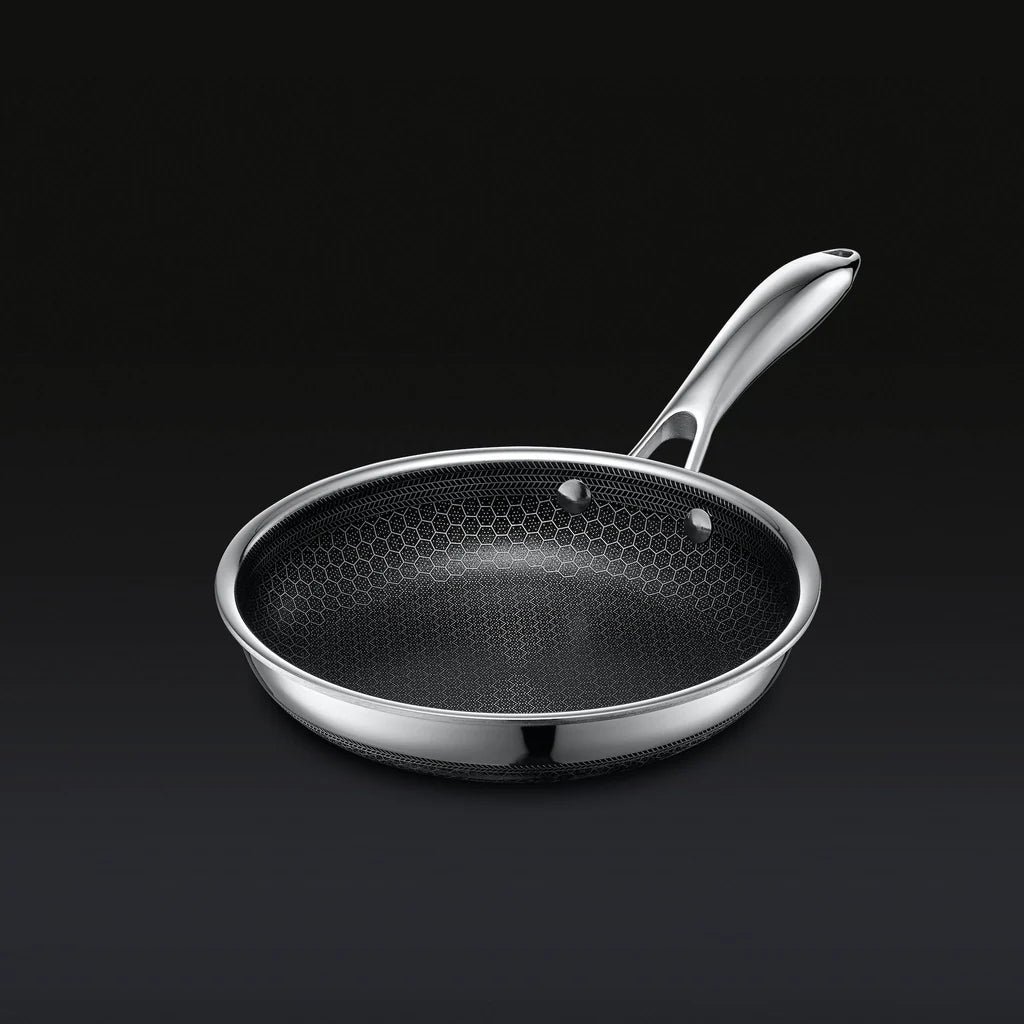 Stainless steel frying pan with a hexagonal-patterned interior on a dark background.