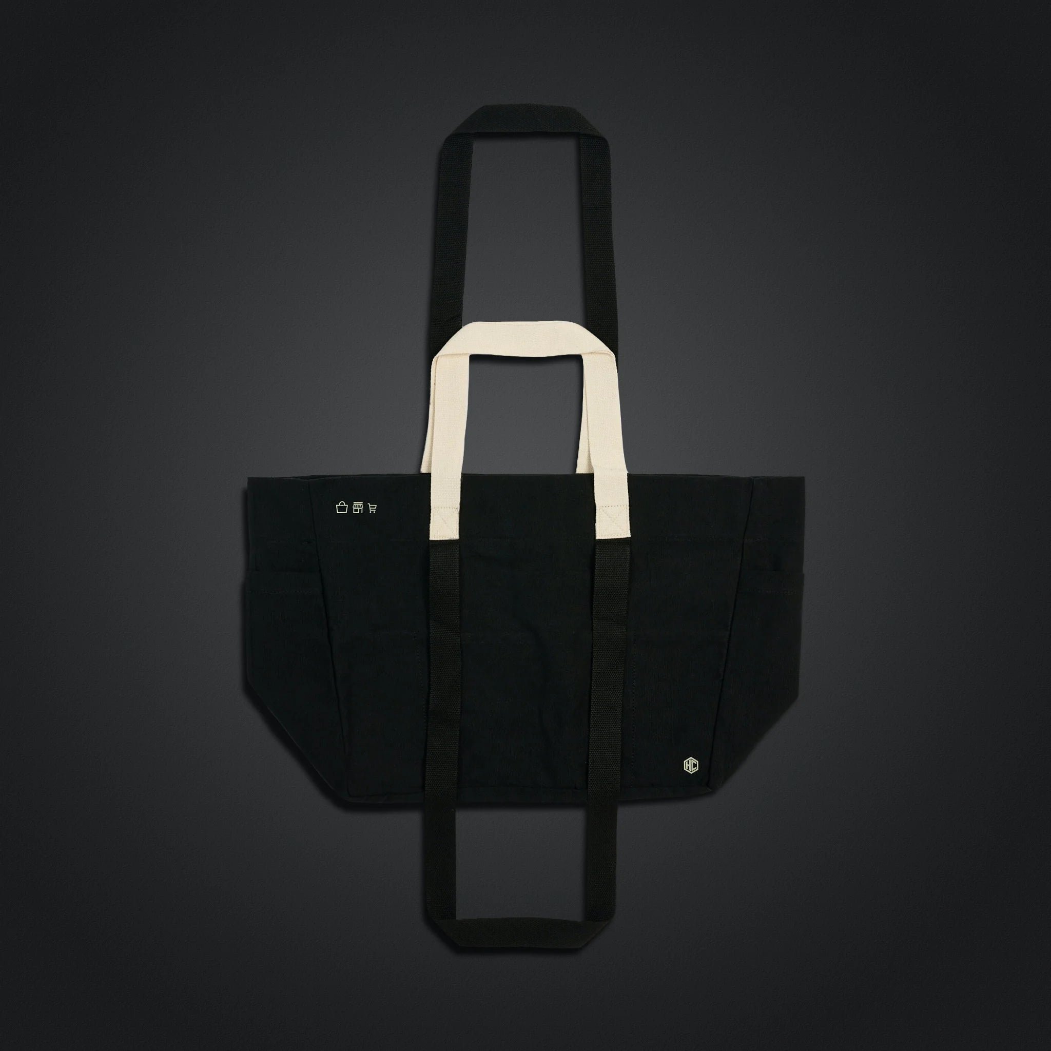 Black tote bag with white handles against a dark background.