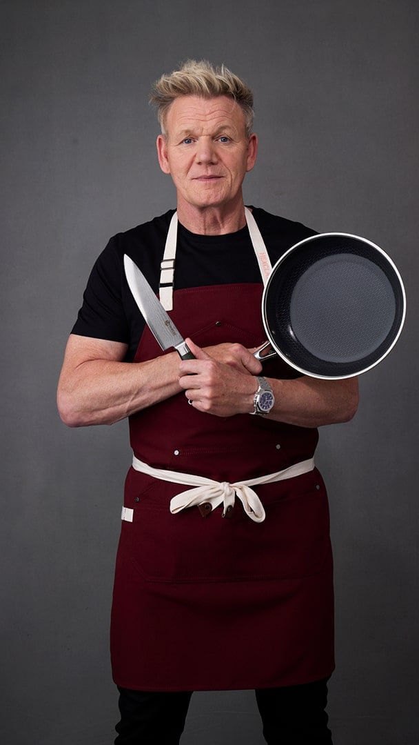A chef in a white uniform holds a frying pan in a professional kitchen.