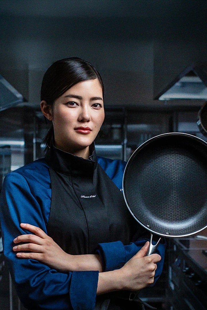 Chef in blue uniform holding a frying pan in a kitchen.