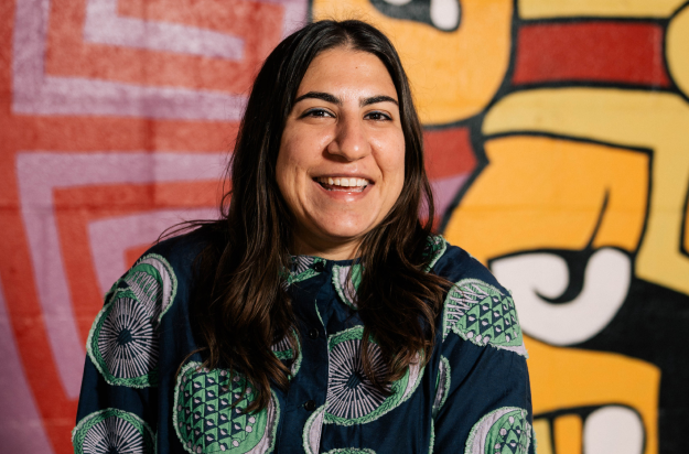 Smiling person in a patterned shirt with a colorful graffiti background.