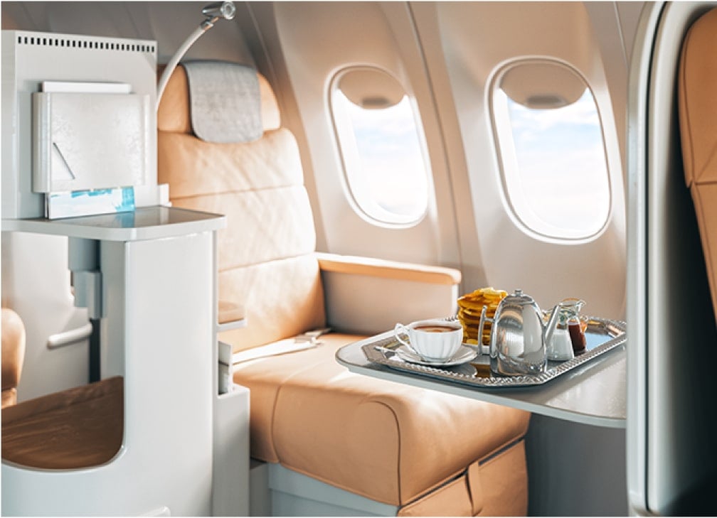 First-class airplane seat with a meal tray containing tea and breakfast items.