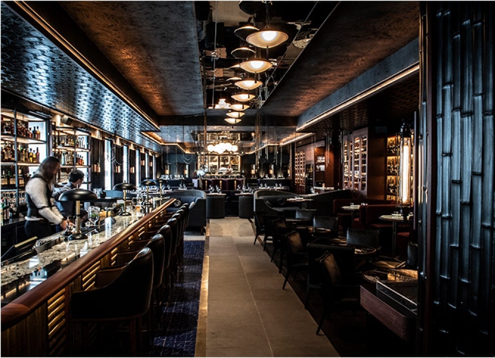 Elegant interior of a dimly lit bar with patrons and bottles lined up against the walls.
