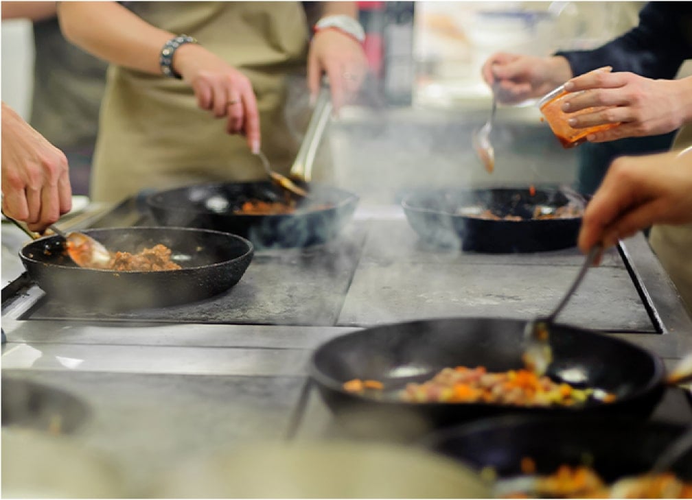 People cooking food in pans on a stovetop.
