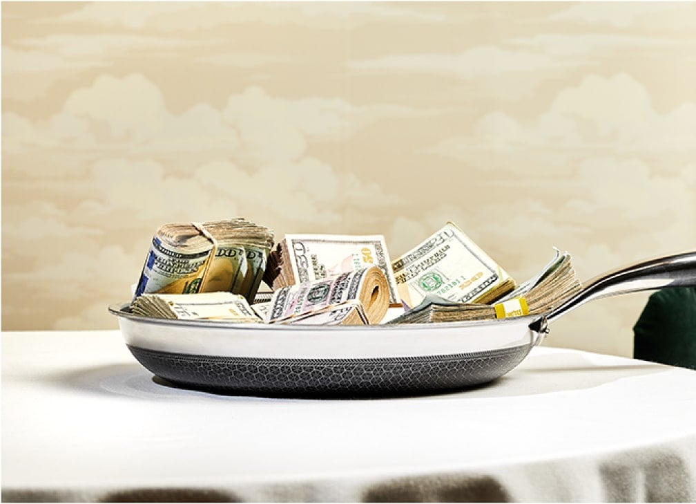 Frying pan filled with stacks of money on a table.