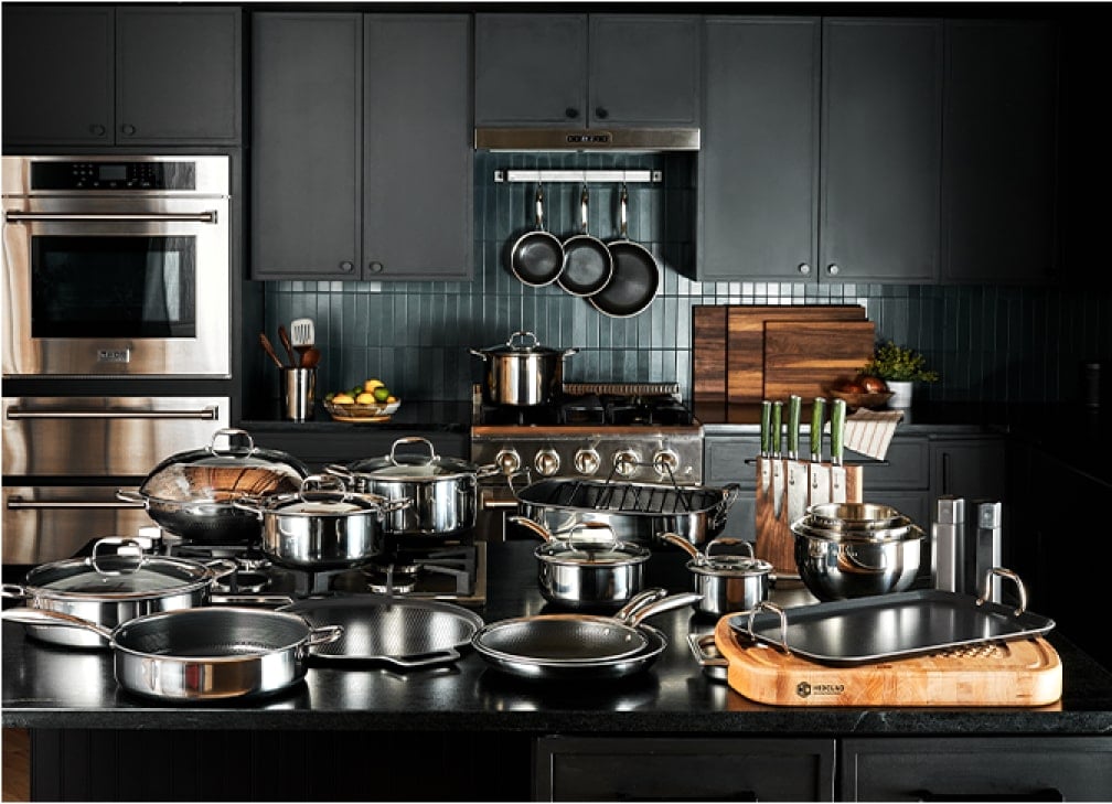 Modern kitchen with stainless steel cookware, utensils, and cutting boards neatly arranged on a black countertop.