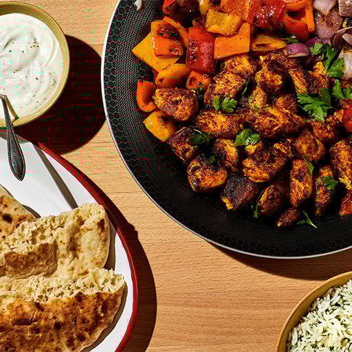 Grilled chicken and vegetables with rice and naan bread on a table.