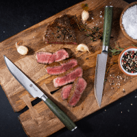 Sliced steak on a wooden cutting board, surrounded by spices and knives.