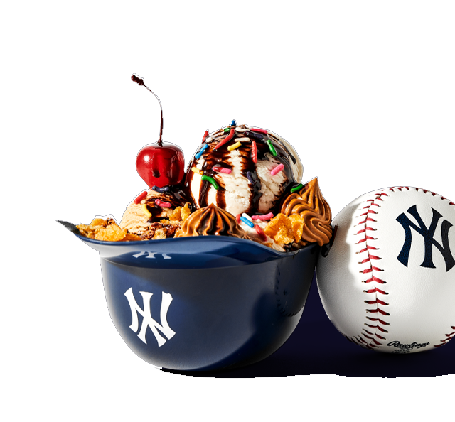 Ice cream sundae with sprinkles and cherry in a baseball helmet next to a baseball.