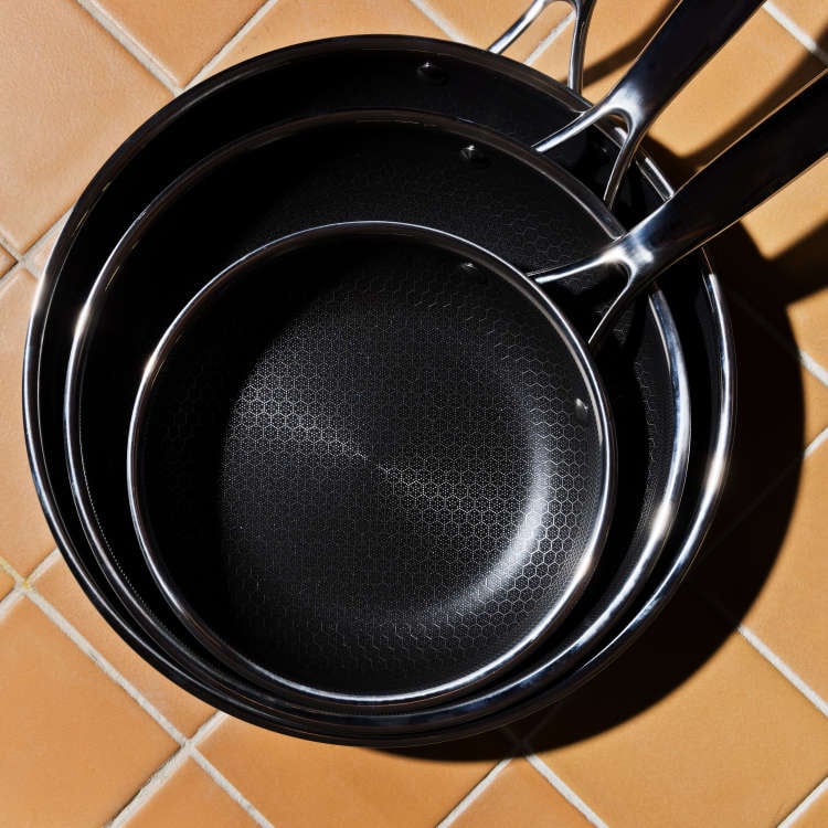 Three stacked nonstick frying pans on a tiled kitchen surface.