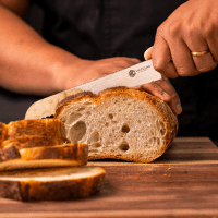 Person slicing a loaf of bread on a wooden cutting board.