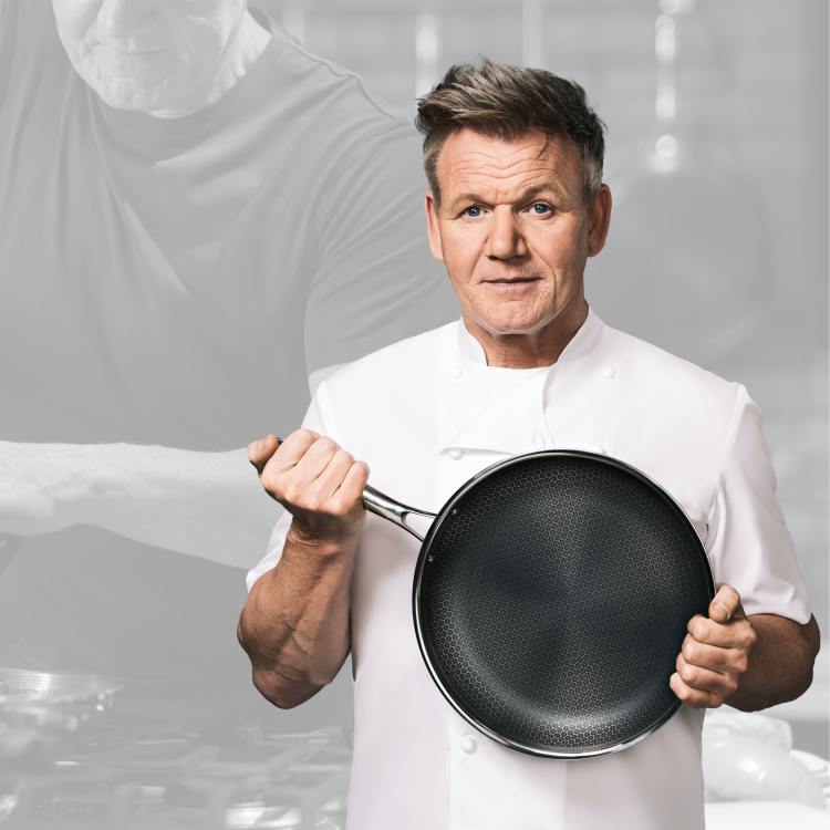 A chef in a white uniform holding a frying pan in a kitchen.