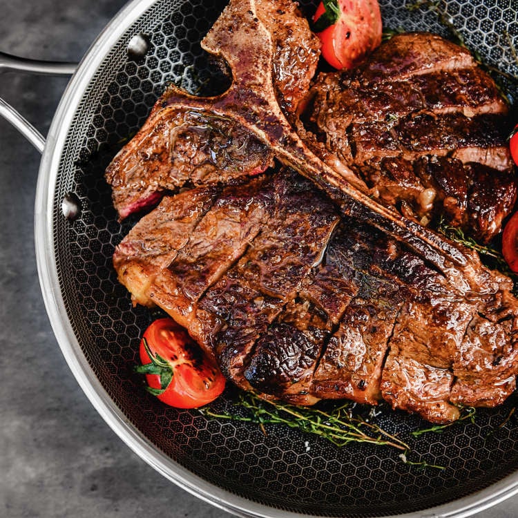 Grilled steak with tomatoes and herbs in a frying pan.