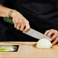 A person is slicing an onion on a wooden cutting board.