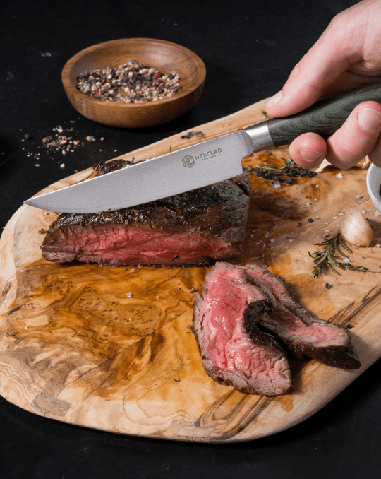 A person slicing a medium-rare steak on a wooden cutting board with a knife.