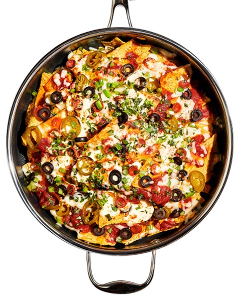 A skillet of loaded nachos topped with cheese, jalapeños, olives, and green onions.