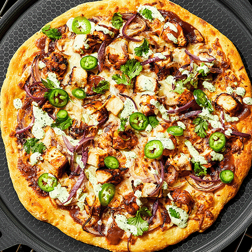 A barbecue chicken pizza with jalapeños and onions on a black surface.