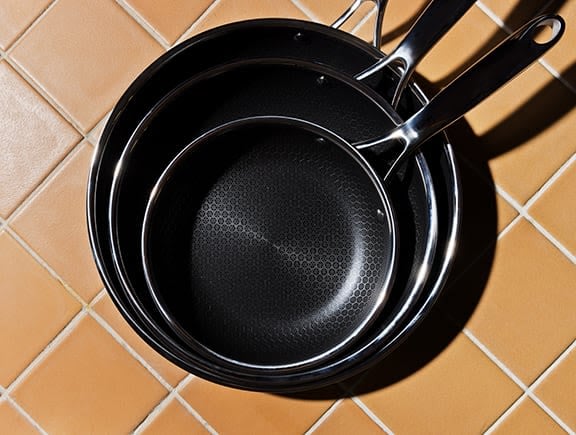 Three stacked frying pans on a tile countertop.