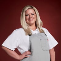 Smiling woman in a white shirt and gray apron against a red background.