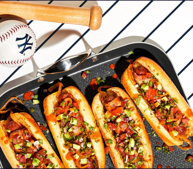 Tray of loaded hot dogs beside a baseball bat and ball.
