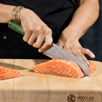 Person cutting raw salmon fillet on a wooden cutting board with a knife.